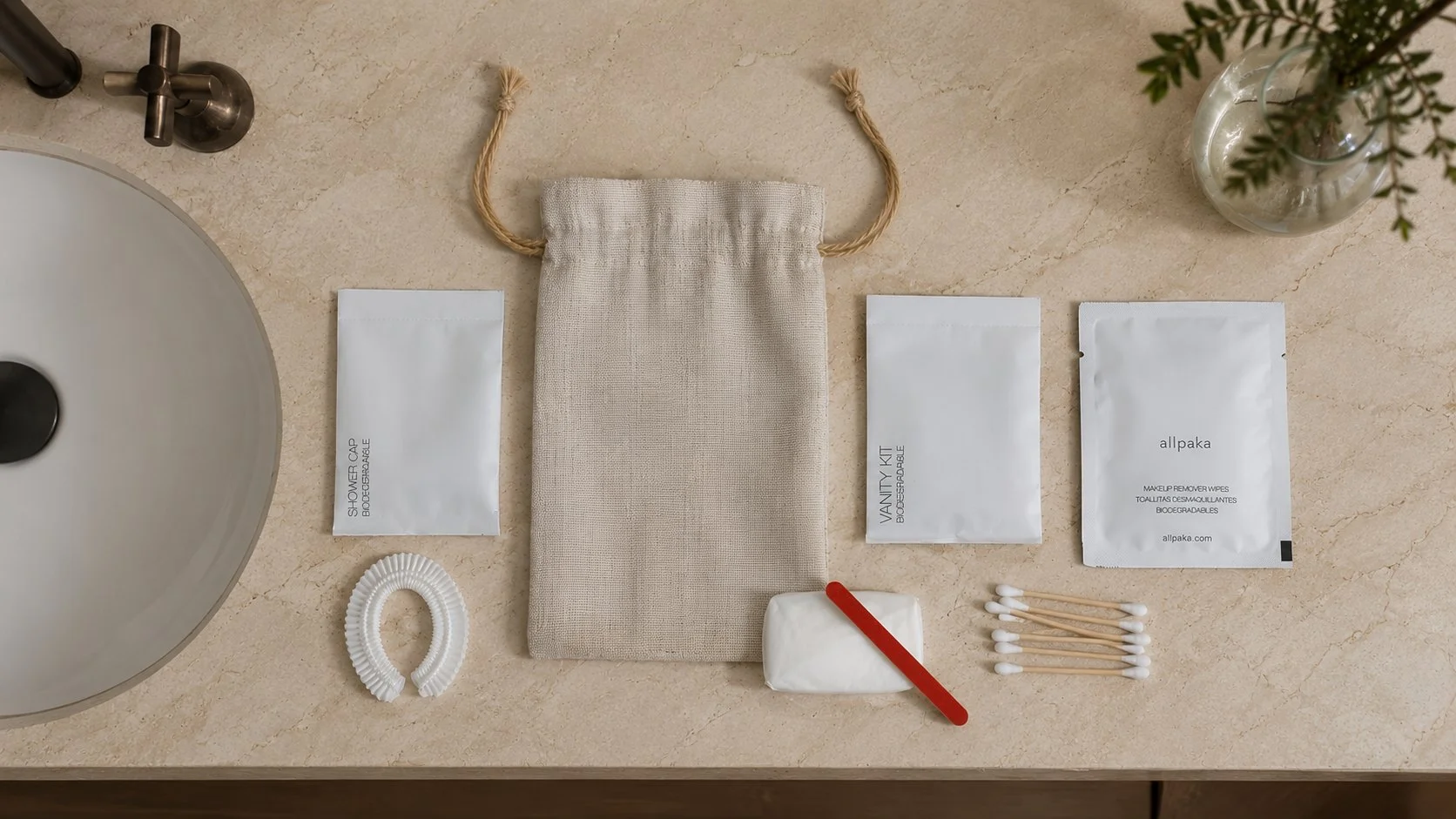Amenities allpaka dispuestos sobre el mesón de un lavamanos: gorra de baño, bolsita de algodón, vanity kit, toallitas desmaquillantes, lima y cotonitos de bambú